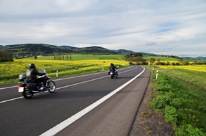 Motorcycles traveling along an empty asphalt road between yellow blooming rape fields